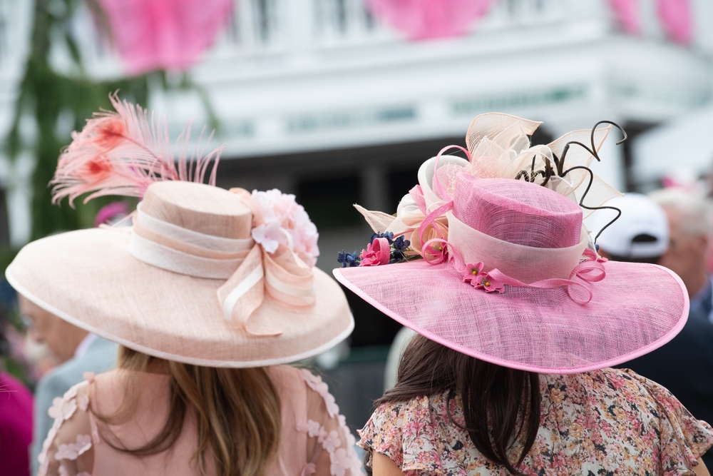 Elegante Damen mit aufwendig gestalteten, floralen Hüten in Rosatönen sind auf dem Weg zu einem royalen Event.