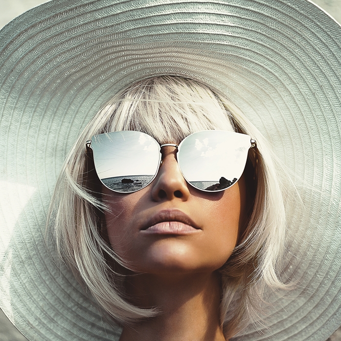 Trendiger Look mit großem weißen Sonnenhut, silbernen Haaren und verspiegelter Statement-Sonnenbrille.