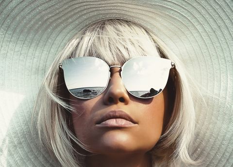 Trendiger Look mit gro&szlig;em wei&szlig;en Sonnenhut, silbernen Haaren und verspiegelter Statement-Sonnenbrille.
