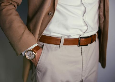 Elegante Outfit-Details eines Herren in braunem Sakko, beiger Hose und mit passender Uhr zum braunen Lederg&uuml;rtel.