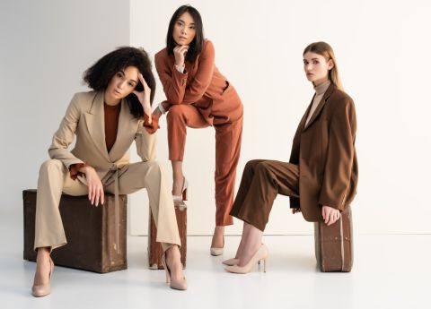 Models pr&auml;sentieren auf Koffern sitzend und lehnend subtil elegante Anz&uuml;ge in Beige- und Braunt&ouml;nen.