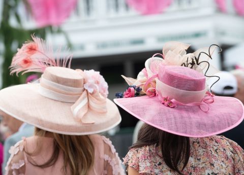 Elegante Damen mit aufwendig gestalteten, floralen H&uuml;ten in Rosat&ouml;nen sind auf dem Weg zu einem royalen Event.